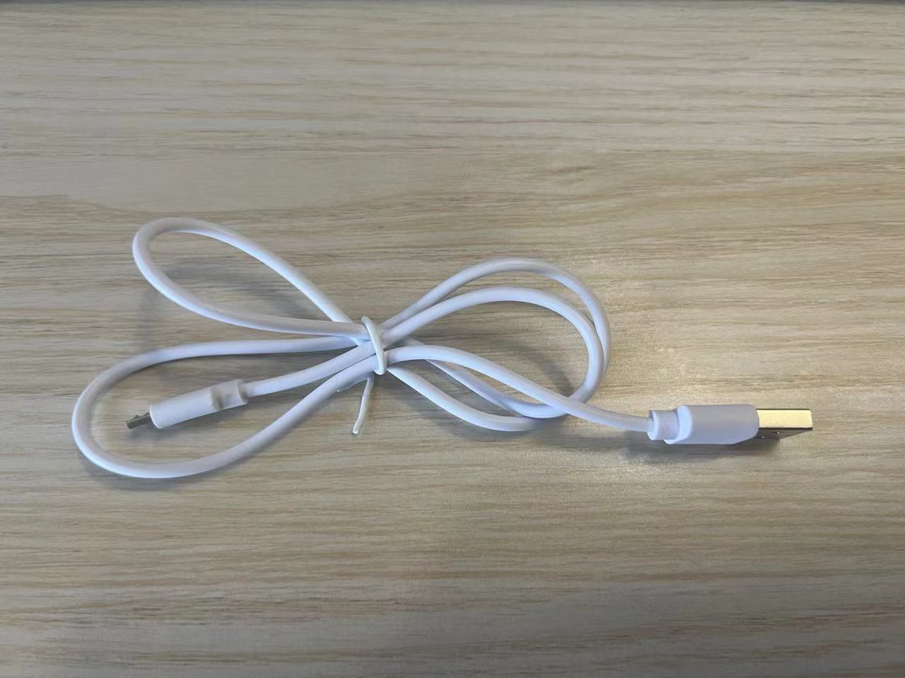 White charging cable on wooden surface, featuring a USB connection for electronic devices.